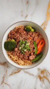 a bowl of ground beef ramen stir-fry, topped with sesame seeds and green onions.
