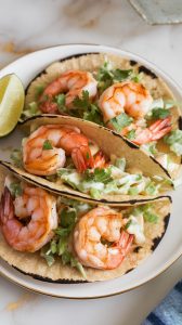 shrimp tacos arranged on a white plate, topped with vibrant cilantro lime slaw and drizzled with a creamy sauce