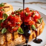 balsamic glaze being drizzled over bruschetta-topped grilled chicken.