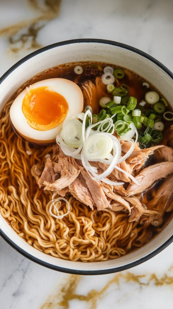 a bowl being assembled – ramen noodles on the bottom, shredded chicken and dark broth being ladled on top, soft-boiled egg and green onions added