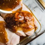 marinade being poured over chicken breasts in a glass dish, with the mixture coating the meat evenly.