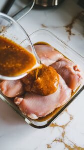 marinade being poured over raw chicken breasts in a shallow glass dish, coating them completely.