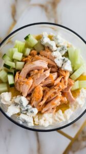 finished bowl with buffalo chicken, diced celery and cucumber, blue cheese crumbles, and a drizzle of olive oil.