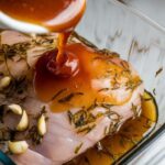 mojo marinade being poured over pork chops in a glass dish, garlic and herbs clinging to the meat.