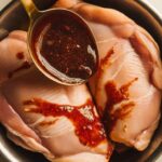 ompleted Moroccan marinade being spooned over raw chicken breasts in a bowl, with marinade clinging to the surface.