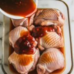 marinade being poured over raw chicken thighs in a glass dish, thick glaze coating each piece.