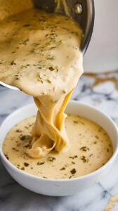 hot queso blanco being poured from a saucepan into a white bowl, thick and creamy with flecks of green chile