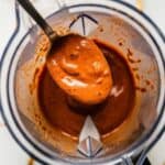 a spoon dipping into blended romesco sauce in the blender, thick creamy sauce clinging to spoon with a glossy finish.