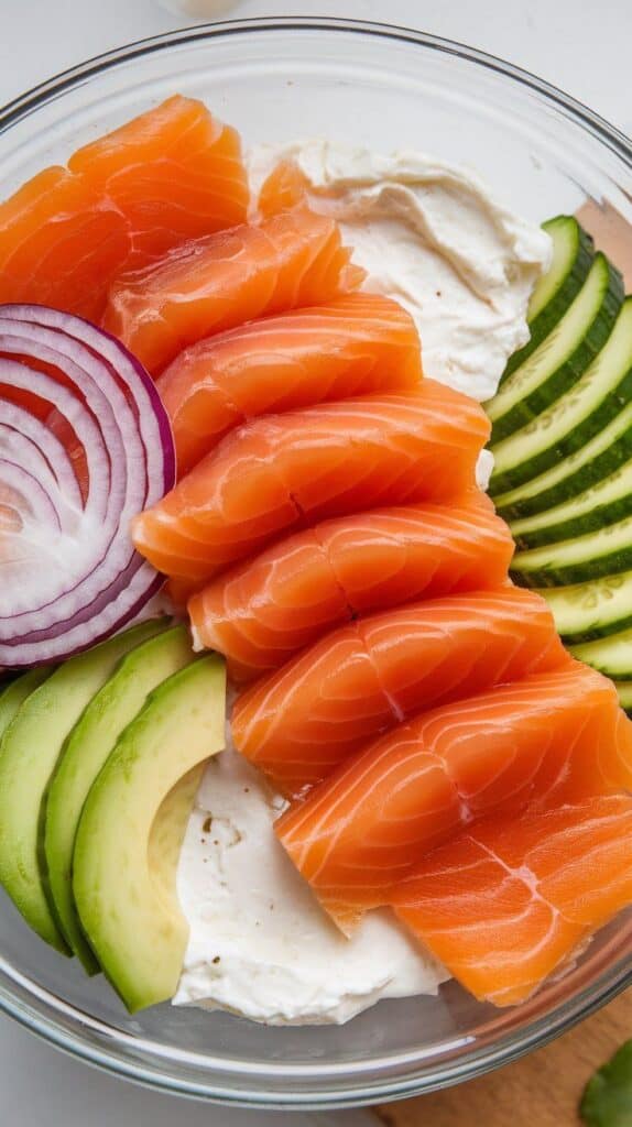 sliced avocado fanned next to thin cucumber rounds and red onion curls in the bowl.