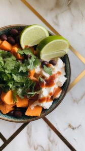 finished bowl with chopped cilantro, lime wedges, and avocado slices over sweet potato, black beans, and cottage cheese.