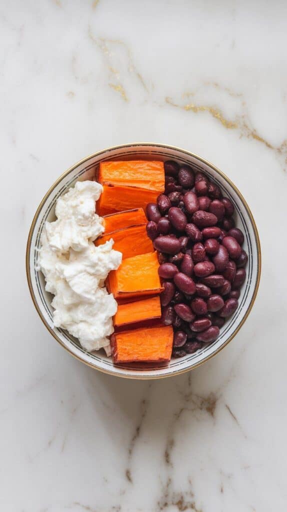 bowl with bright roasted sweet potatoes and black beans nestled next to cottage cheese, ingredients layered cleanly.