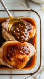 thick marinade being spooned over chicken thighs in a glass dish, rich brown glaze coating the meat evenly.