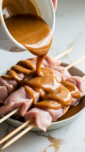 marinade being poured over raw chicken skewers in a shallow dish, thick sauce coating the meat evenly