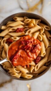sun-dried tomato cottage cheese sauce being spooned over penne pasta, thick and creamy, sauce clinging to the pasta.