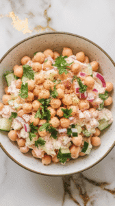 finished chickpea and cottage cheese salad served in a wide white bowl, colorful and creamy with chickpeas and diced vegetables, sprinkled with cracked pepper and parsley,