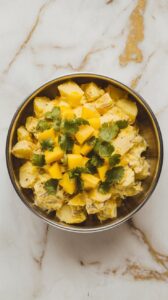 finished coconut curry potato salad with mango in a shallow serving bowl, bright yellow with diced mango and chopped cilantro on top