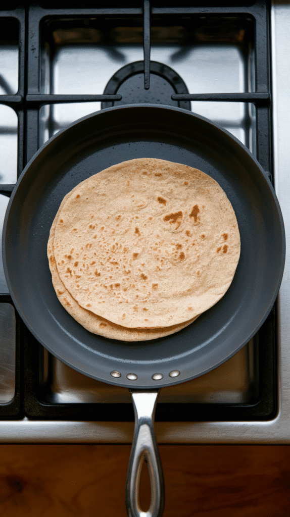 soft whole wheat wraps being warmed on a clean skillet, just slightly puffed and pliable, on a modern stainless steel gas stove,