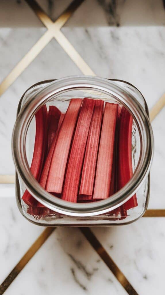 neatly sliced rhubarb batons being packed vertically into a clear glass jar, colorful ends peeking out at the top