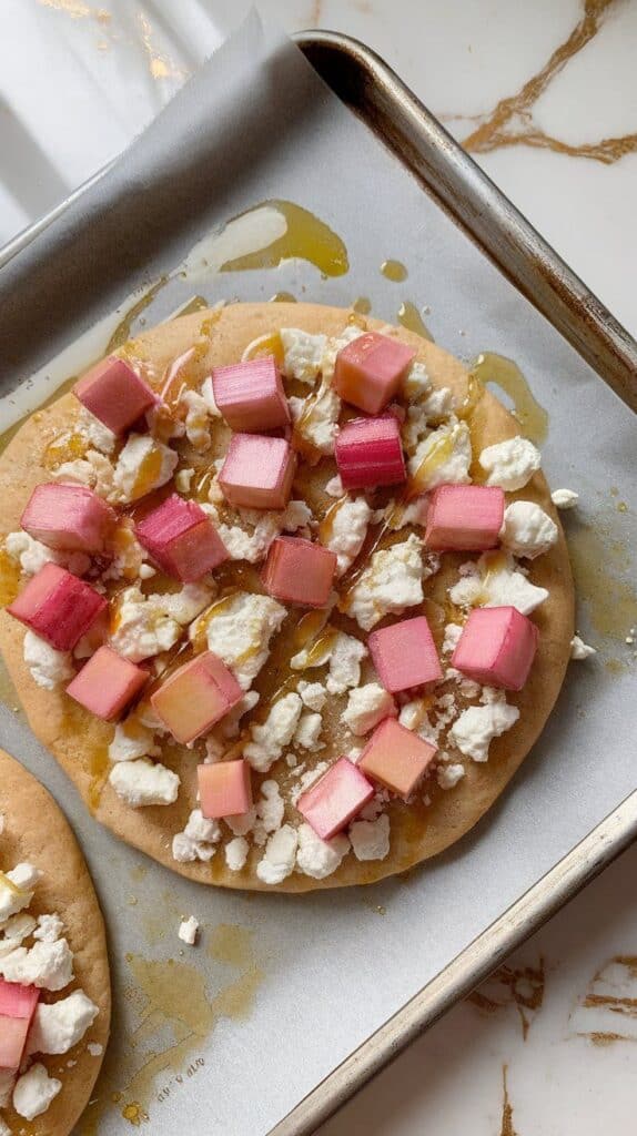 flatbread topped with crumbled goat cheese, pink rhubarb slices, and honey drizzle just before baking