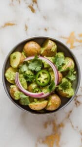 finished salsa verde roasted potato salad in a shallow serving bowl, garnished with cilantro, red onion, and jalapeños, bright green sauce visible