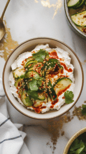 a finished smashed cucumber cottage cheese bowl with creamy white cottage cheese topped with chili-glossed cucumbers, sesame seeds and cilantro scattered on top