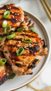 grilled charred scallion chicken thighs on a white ceramic plate, sliced and garnished with raw scallion curls and a drizzle of leftover (cooked) marinade