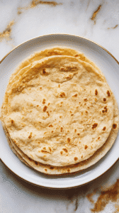 two finished cottage cheese flatbread wraps stacked on a white plate, soft and slightly golden, flecks of oat flour visible