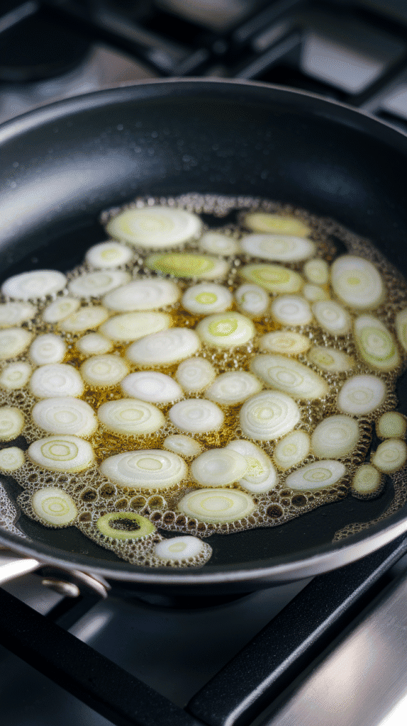 scallion whites sizzling in hot oil, tiny bubbles forming around the edges, scallions just turning golden.