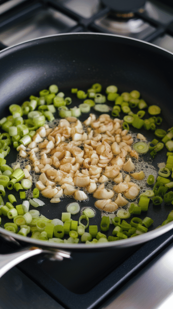 garlic and scallions sautéing in oil, garlic just starting to brown, scallions bright green and sizzling.