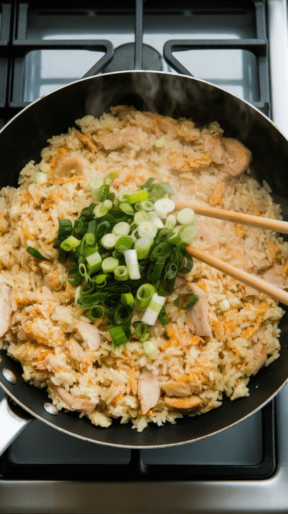 sliced green onions being tossed into hot lemongrass chicken fried rice, steam still rising, bits of chicken and egg visible throughou