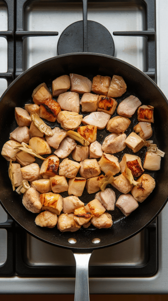 diced chicken sizzling in a skillet with golden lemongrass, garlic, and ginger, slightly caramelized edges starting to form.