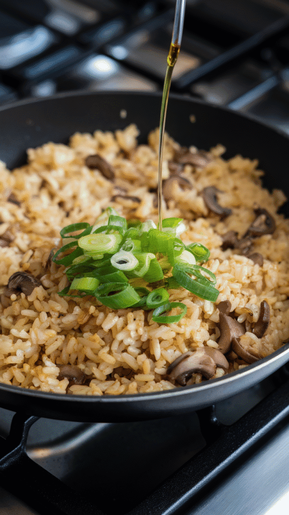 thin green onion slices and a drizzle of truffle oil being folded into golden mushroom fried rice, everything glistening slightly.