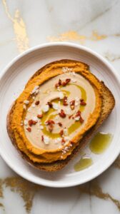 A plate with a slice of bread with hummus and nuts.